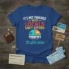 T-shirt with "It's Not Paradise When Locals Can't Afford To Live Here" text and city skyline graphic
