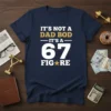 Navy t-shirt with white and gold text: "IT'S NOT A DAD BOD IT'S A 67 FIG★RE" in bold, fun typography