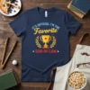 Navy t-shirt with "It's Official I'm The Favorite Son-In-Law" text and a golden trophy graphic surrounded by laurel leaves