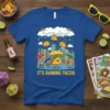 It's Raining Tacos t-shirt with cartoon tacos falling from a rainbow cloud over a city, kids holding umbrellas