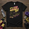 It's Step Aerobics Day! text with silhouetted figures on aerobic steps, vibrant pink and yellow design on black t-shirt