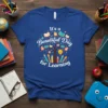 It's a Beautiful Day for Learning quote on a blue t-shirt with a tree graphic featuring books, pencils, and a