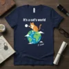 It's a cat's world t-shirt featuring an orange tabby cat sitting on planet Earth, with text above and a signature