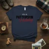 Navy blue t-shirt with "It's A PATTERSON Holiday" text in black and red, featuring a paw print accent