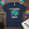 T-shirt design with white text "IT'S A REASON I FIDGETS" above a brain graphic filled with pop-it toy bubbles