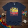 It's A Trini Thing You Wouldn't Understand text with carnival graphics on a navy blue t-shirt