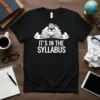 Black t-shirt with white text "IT'S IN THE SYLLABUS" and graphic of open book, brain, glasses, and scrolls