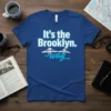 Blue t-shirt with white and light blue text "It's the Brooklyn. way" and a graphic of the Brooklyn Bridge