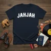 Navy blue t-shirt with white bold arched text spelling "JAHJAH" on a wooden background with travel accessories