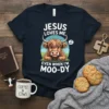 Jesus Loves Me Even When I'm Moo-dy t-shirt with a cute cartoon Highland cow graphic and white text