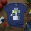 White text "JUST DODGE IT BRO" with a neon green dodgeball in motion on a navy blue t-shirt