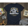 T-shirt with white text "JUST ONE MORE GRANDCHILD I Promise" and golden apple tree graphic