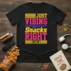 T-shirt with bold yellow and pink text reading "JUST VIBING WITH Snacks RIGHT NOW" on a black shirt