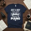 Just A Boy Who Loves Playing The Piano text design with piano keys graphic on a navy blue t-shirt