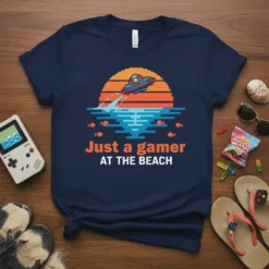 Navy blue t-shirt with "Just a gamer AT THE BEACH" text in orange and white, above a pixel art sunset