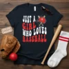 JUST A GIRL WHO LOVES BASEBALL text with a baseball cap graphic on a dark t-shirt