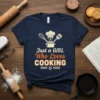 Just a Girl Who LOVES COOKING text design with chef hat, pot, whisk, and spatula graphics on a navy t-shirt