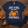 T-shirt graphic with text "Just A Girl Who Loves Football" featuring a football, pumpkin, and helmet, set against fall leaves