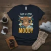 Highland cow graphic with text "Just a Little MOODY" on a navy t-shirt, featuring stormy weather elements