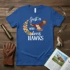 Just a WHO loves HAWKS text with a flying hawk graphic and heart shapes on a blue t-shirt