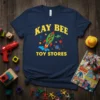 Navy blue t-shirt with yellow text "KAY BEE TOY STORES" and a green rocket ship with animal characters flying through