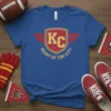 Royal blue t-shirt with "KC Heart of the City" text and shield graphic in yellow and red, Kansas City fan
