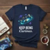 Keep Being Curious t-shirt with telescope and galaxy design, featuring planets and swirling stars
