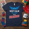 Keep Calm My Son Is A Superhero text design with blue wings and mask graphic on navy t-shirt