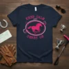 Keep Calm and Derby On text with a pink running horse graphic on a navy t-shirt, equestrian theme