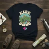 Keep Going text with a graphic of a hiker on a mountain trail, river, and sun on a dark t-shirt