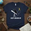 Keep Looking Up t-shirt design with a black cat sitting on a telescope under a crescent moon and stars