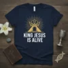 Navy t-shirt with "KING JESUS IS ALIVE" text, a golden crown, and a glowing archway representing resurrection