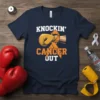 Navy t-shirt with "KNOCKIN' CANCER OUT" text, orange ribbon, and boxing glove graphic