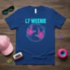 L7 WEENIE text with retro graphics and hand gestures on a blue t-shirt. Features pink and teal colors