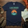 Lakewood Colorado text above a mountain and lake graphic with pine trees, on a navy blue t-shirt