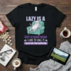 Black t-shirt with a cartoon sloth sitting on a couch holding a remote, with the text "LAZY IS A VERY