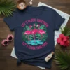 Let's Flock Together text with three pink flamingos and tropical leaves graphic on a navy t-shirt
