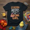 Black t-shirt with bold orange and white text reading "LEUKEMIA MESSED WITH THE WRONG GIRL" and a graphic of a