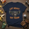 Lift Heavy Eat Trash t-shirt design with a muscular raccoon lifting a barbell filled with trash