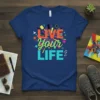 Live Your Life quote in colorful, energetic typography on a navy blue t-shirt, featuring abstract shapes and music notes