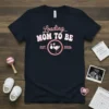 Loading... Mom To Be Est. 2026 t-shirt with a stork graphic carrying a baby bundle