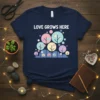 Navy t-shirt with white text "LOVE GROWS HERE" above a pastel graphic of trees and circles