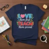 LOVE them first TEACH them second quote on a navy t-shirt with colorful pencils and heart graphic