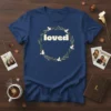 Navy blue t-shirt with the word "loved" in bold white letters inside a green wreath with white doves