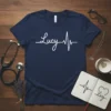 Navy blue t-shirt with white script text "Lucy" integrated into a heartbeat EKG line design, primary keyword Lucy Heartbeat T-Shirt