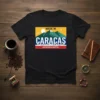 T-shirt with "MADE IN CARACAS HECHO EN LA CAPITAL" text, mountains, sun, and city skyline graphic