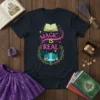Magic Is Real text with open book and forest waterfall graphic on a dark t-shirt