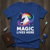 Blue t-shirt with white text "MAGIC LIVES HERE" above a rainbow-maned unicorn illustration in a starry sky