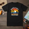 Manila Bay Philippines text with a retro sunset, palm trees, a couple, and a dolphin graphic on a black t-shirt