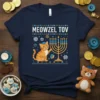 Meowzel Tov Hanukkah t-shirt featuring an orange cat, menorah, dreidel, and snowflakes